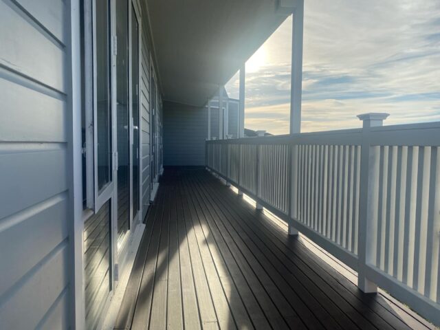 photo shows a front deck of a house with a white balustrade, with the sun beaming in